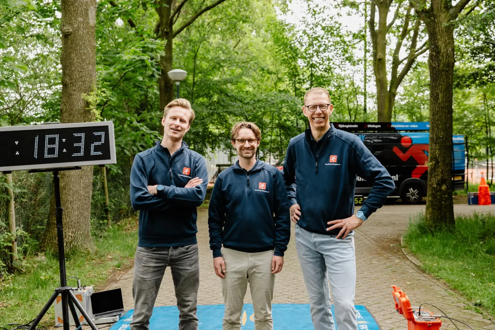 Drie teamleden van Hardloopuitslagen.nl bij de wedstrijdklok en tijdwaarnemingsmat